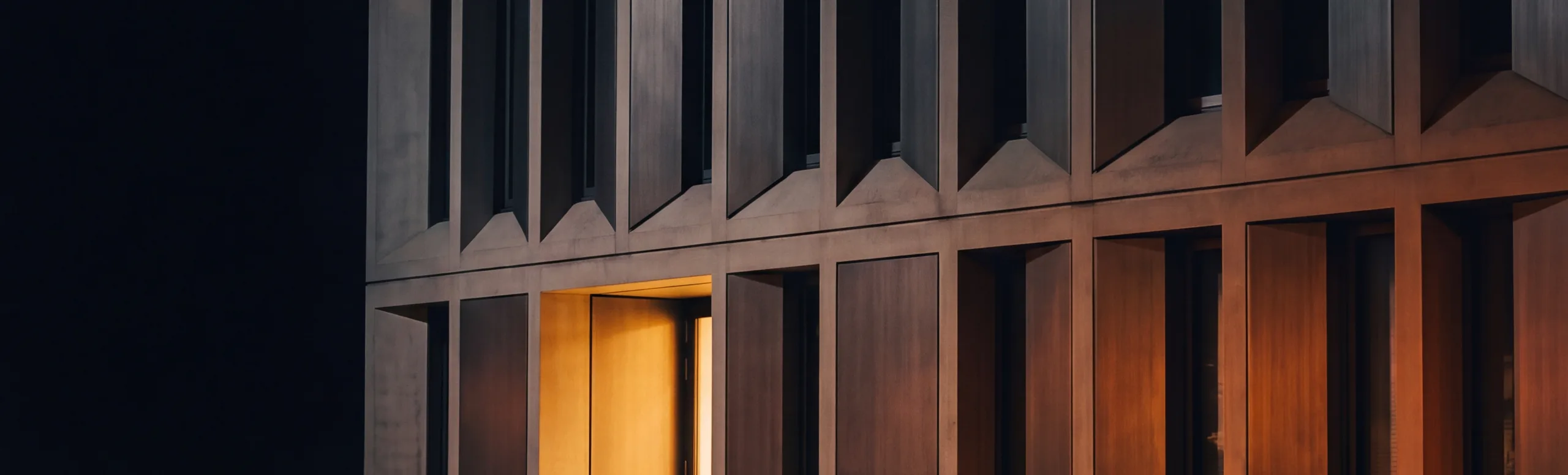 A fachada de um edifício à noite, com uma entrada iluminada ao nível do chão.